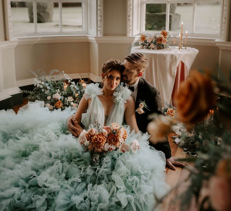 Bride in a light blue wedding dress holding her cafe au late wedding bouquet as she sits with her groom in a tuxedo at Newburgh Priory