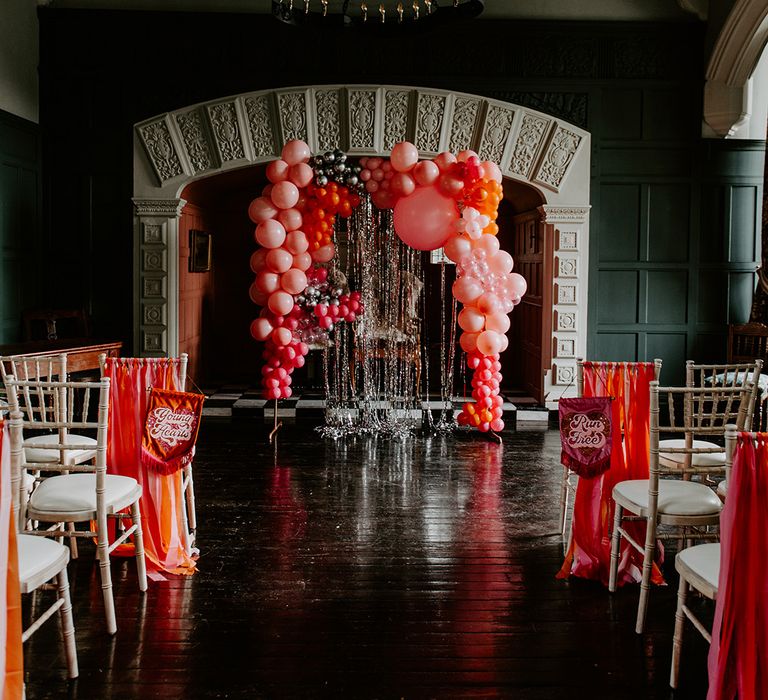 Highfield House wedding venue aisle wedding decor with vibrant red balloon installation, tinsel backdrop and banner chair backs 