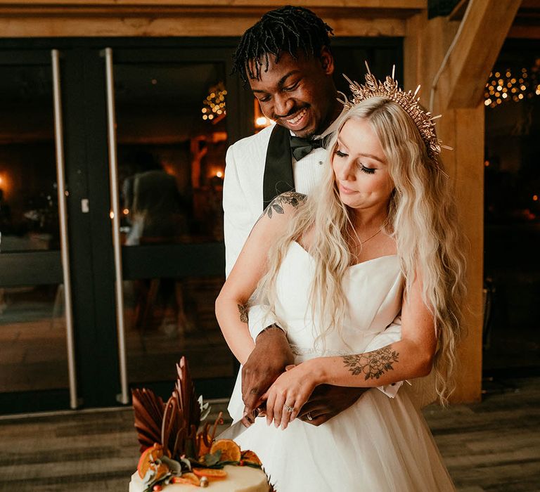 Bride in gold wedding crown cuts the cake with her new husband