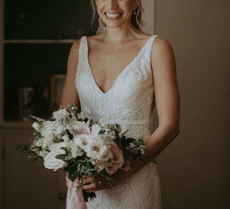 Smiling bride in v-neck lace wedding dress with pink and white wedding bouquet and blonde hair in updo