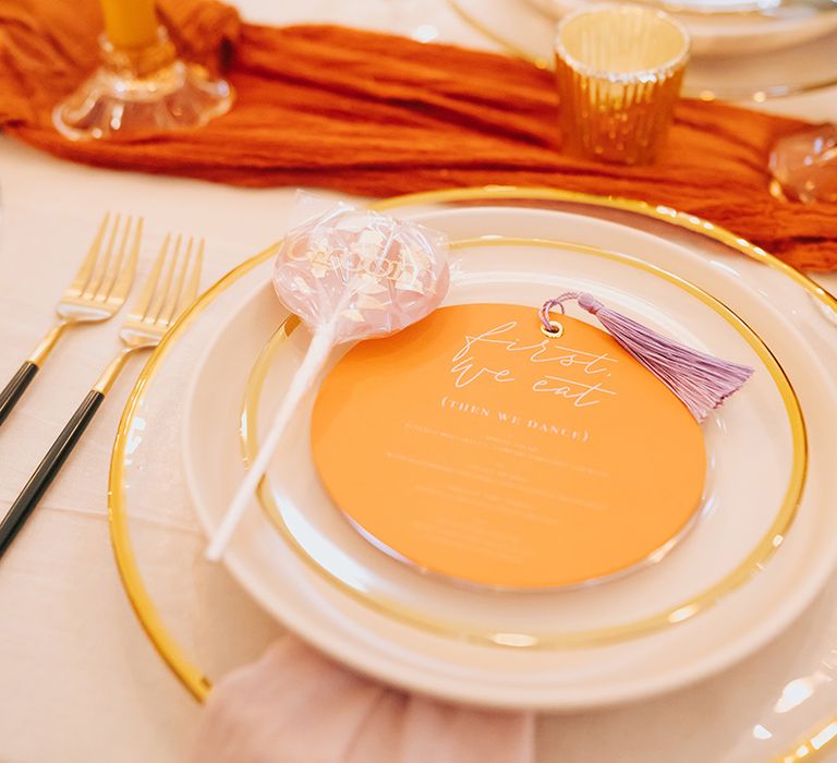 Gold rimmed charger plates with gold cutlery and orange menu card for elegant place setting 