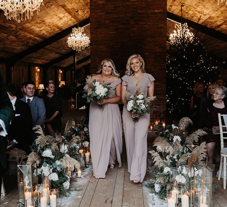 Two bridesmaids in taupe outfits walk down the aisle together for winter wedding at the Lake District