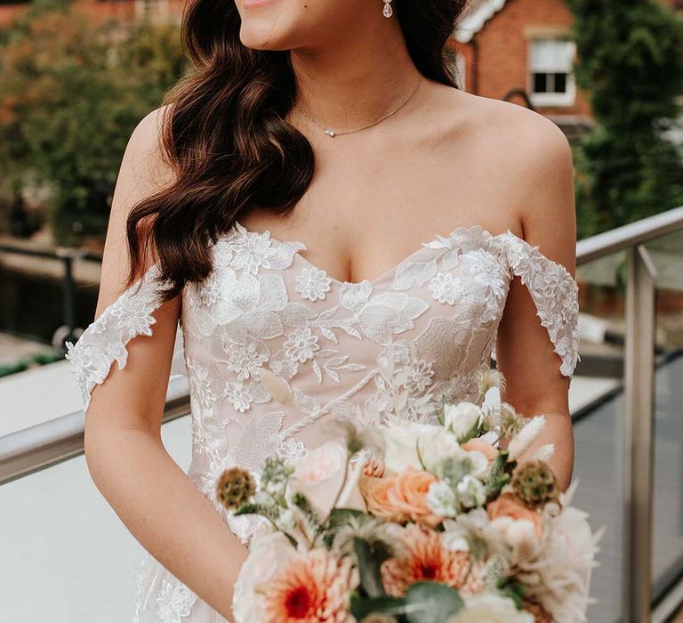 Bride with curled sideswept hair and silver hair accessory with sweetheart off the shoulder flower lace wedding dress and orange wedding bouquet