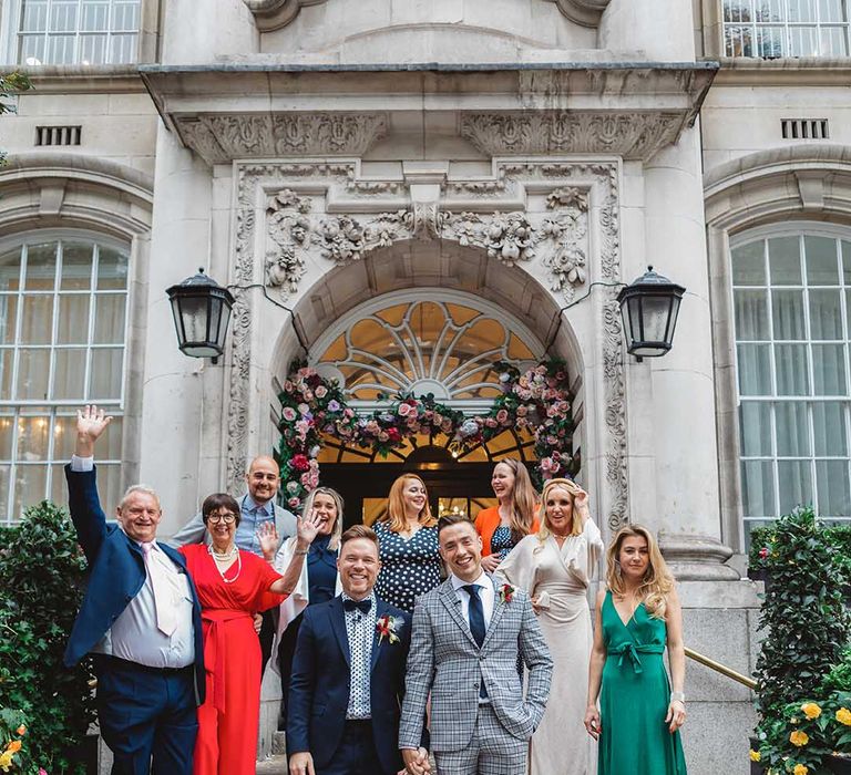 Grooms stand with their wedding guests outdoors on steps 