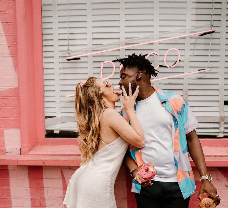 fun city elopement with bride in a short wedding dress and groom in a patterned shirt eating doughnuts 