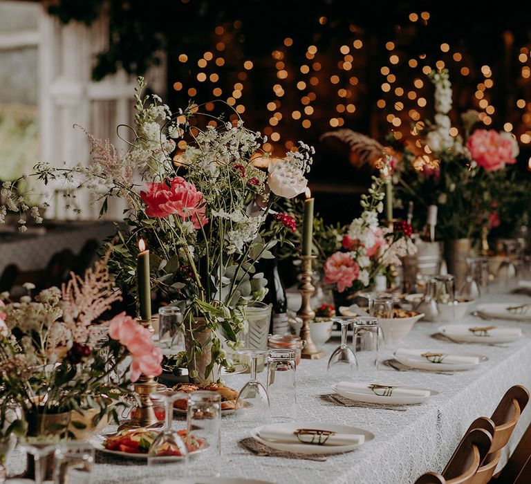 Table setting with patterned tablecloth, green candles in gold candleholders and pink, red and white flowers