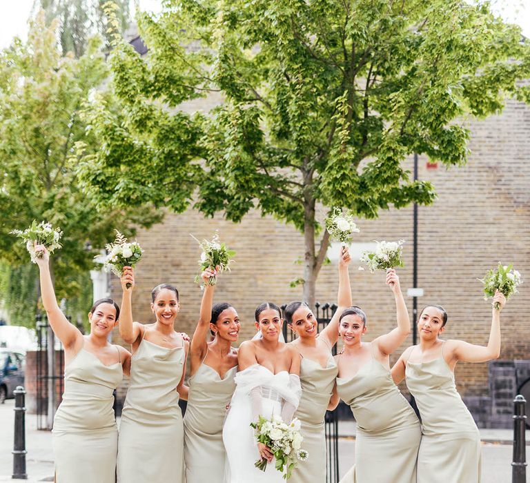 Bridesmaids with slicked back hair in sage green cowl neck satin dresses with bride in off the shoulder corset style wedding dress