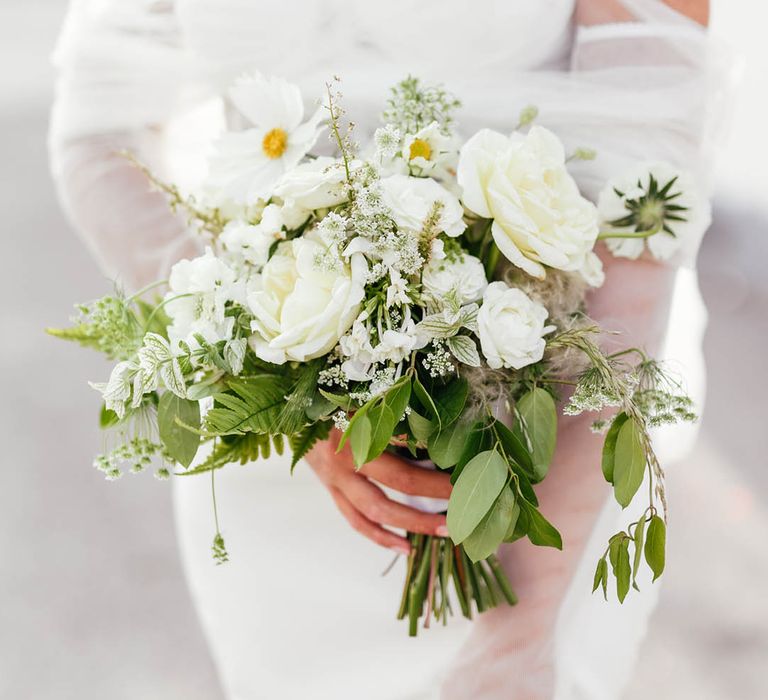 Bride holds white flower wedding bouquet in off the shoulder white wedding dress