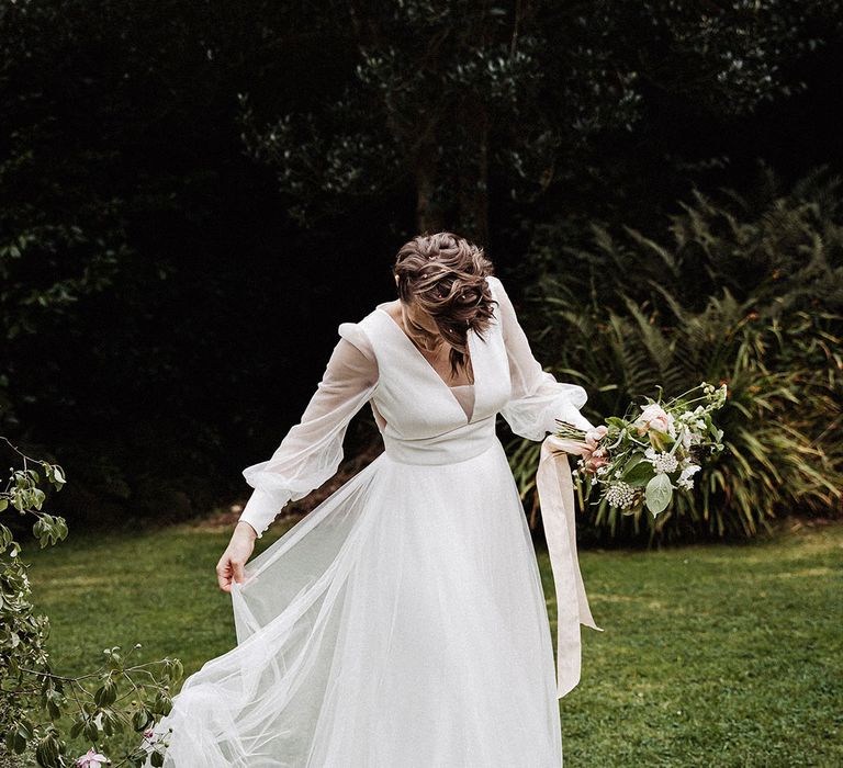 Bride in sheer long sleeved wedding dress with tulle skirt and pink and white bouquet