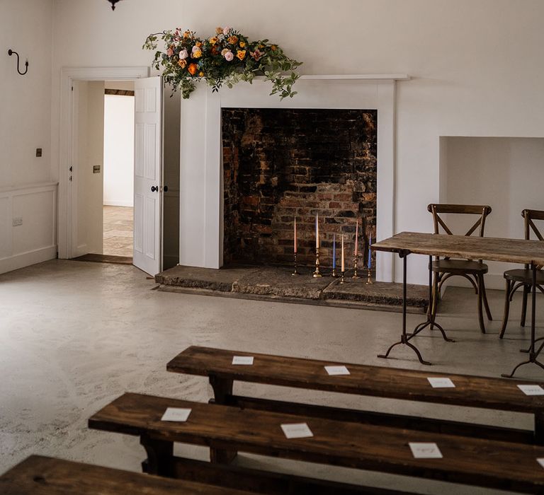 Aswarby Rectory ceremony room with colourful taper candles in the fireplace with yellow, orange, pink and blue flowers 