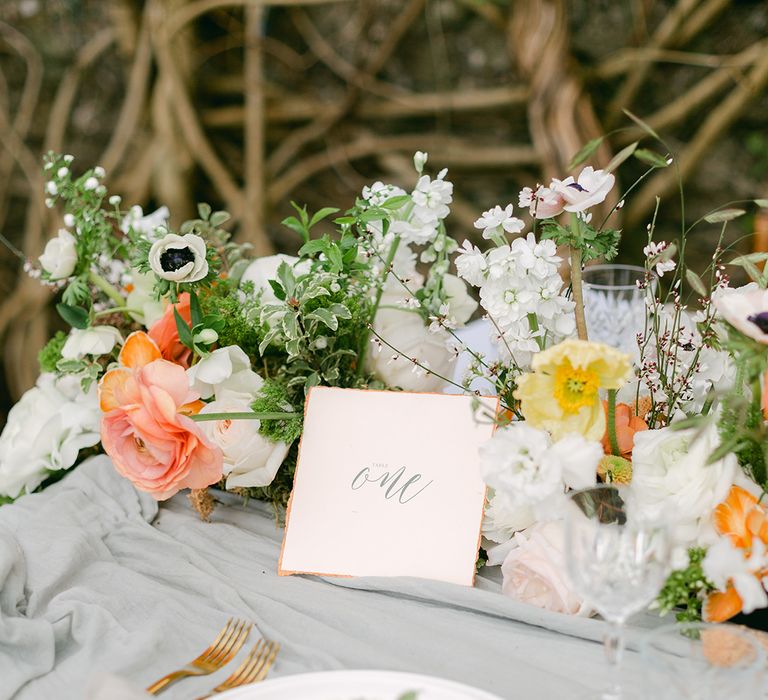 romantic place setting with gold cutlery, calligraphy table name sign and peach and white wedding flowers 