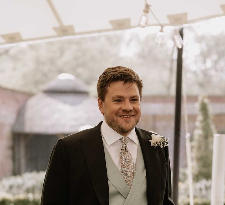 Groom smiles in black morning suit with puppytooth trousers, mint green waistcoat and patterned tie 