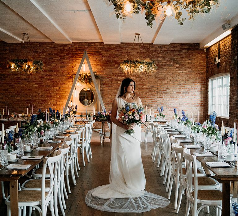 Bride in one shoulder wedding dress with a long veil holding colourful bouquet that matches the wedding flowers decorating the Larkspur Lodge wedding venue 