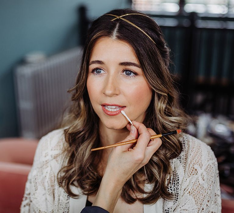 Bride wearing a gold hair piece gets her makeup done for her wedding day