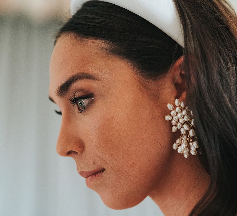 Bride wearing statement pearl earrings with curled brown hair and a chunky white headband and brown winged eyeliner 