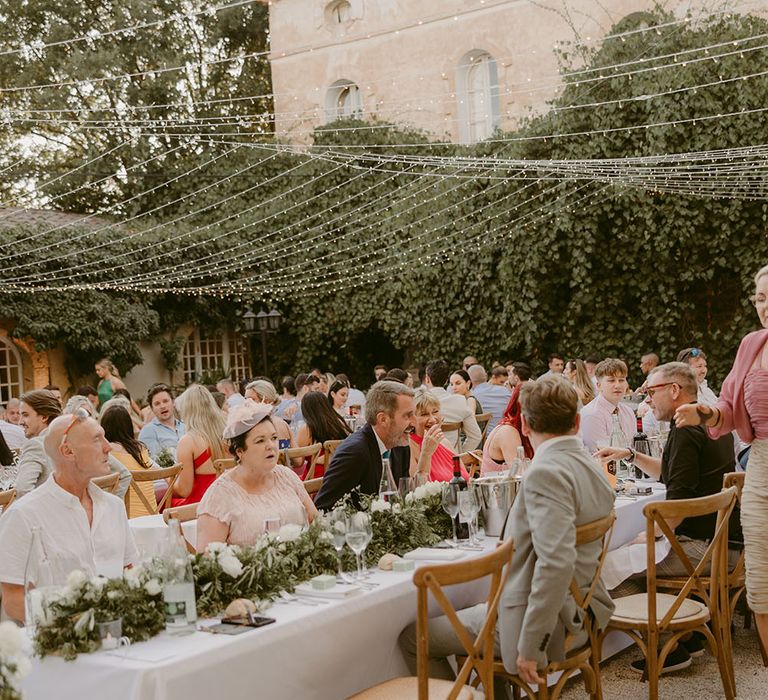 Fairy light canopy hangs above outdoor wedding reception complete with banquet tables and floral table runners 