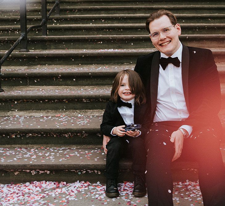 Groom wears black-tie suit and sits with his son on steps for city wedding in London