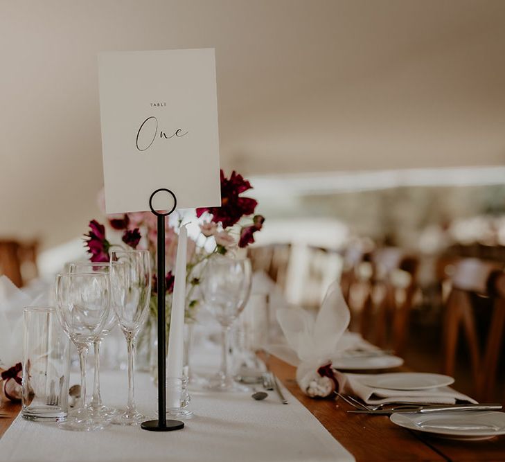 White wedding stationery complete with black calligraphy writing on wooden banquet tables in marquee 