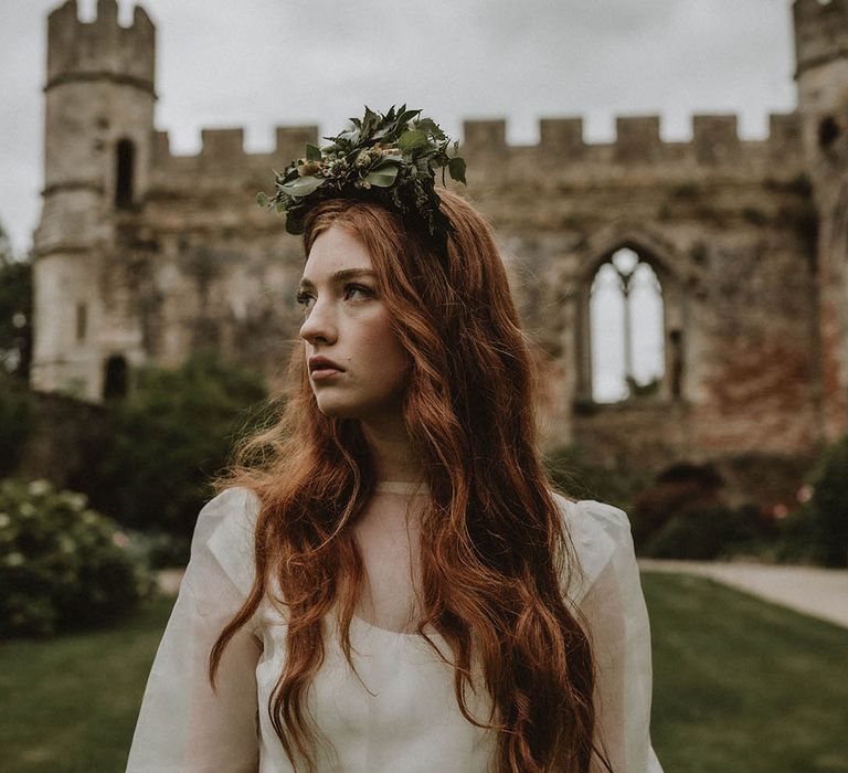 Bride in a wedding dress with sheer top layer wearing a foliage flower crown standing in the gardens at Bishop's Palace, Wells