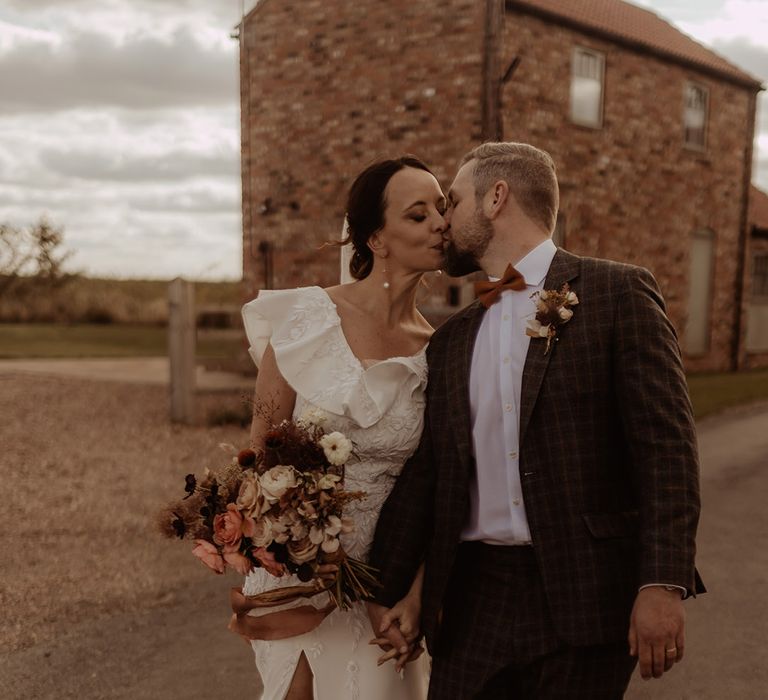 Groom in grey checkered custom suit walks kissing the bride for their couple portraits