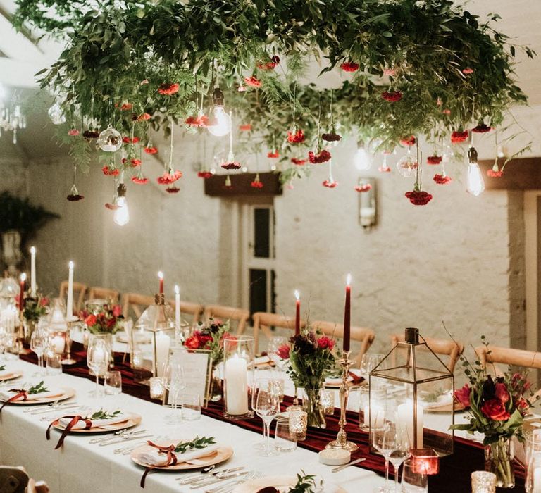 Red taper candles for a red, white and green tablescape with a hanging wreath of foliage and red flowers