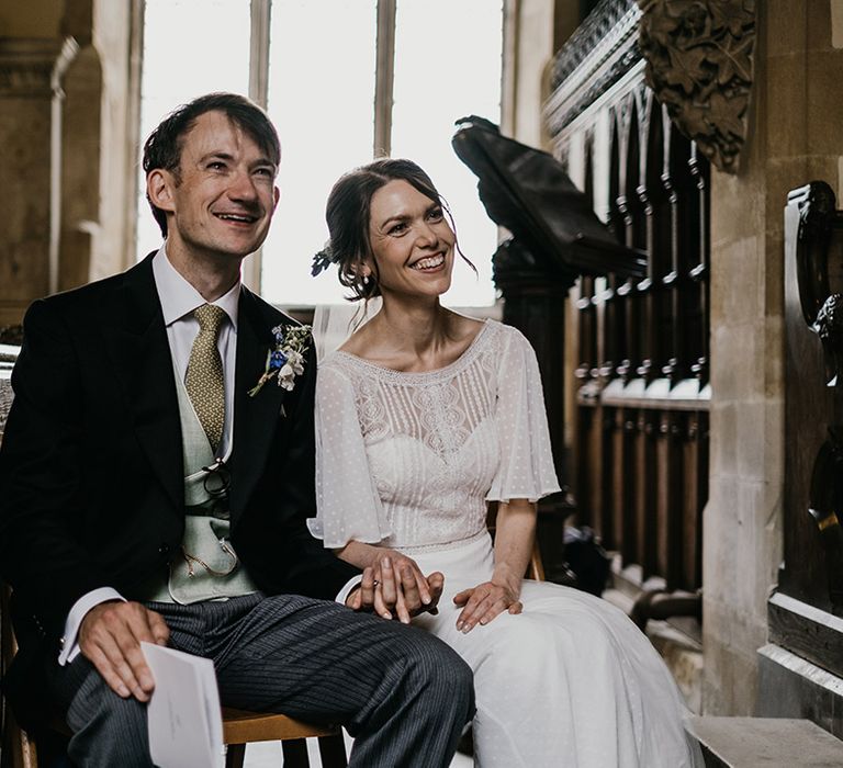 Bride and groom sitting down holding hands in the church at Kelmarsh Hall wedding venue