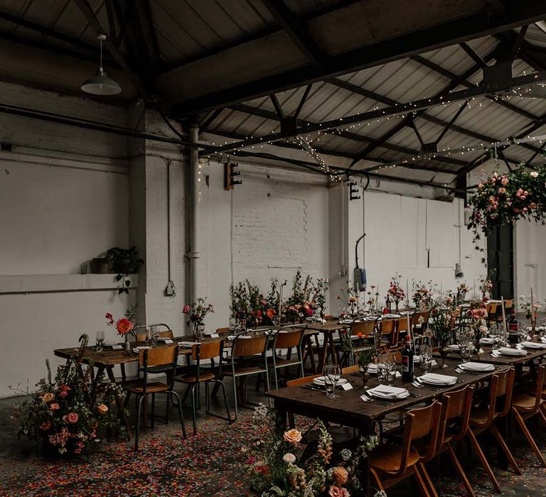 Neutral, minimalistic wedding tablescapes at Hackney Studios with large foliage decor with pops of colour, tapered candles and confetti on the floor