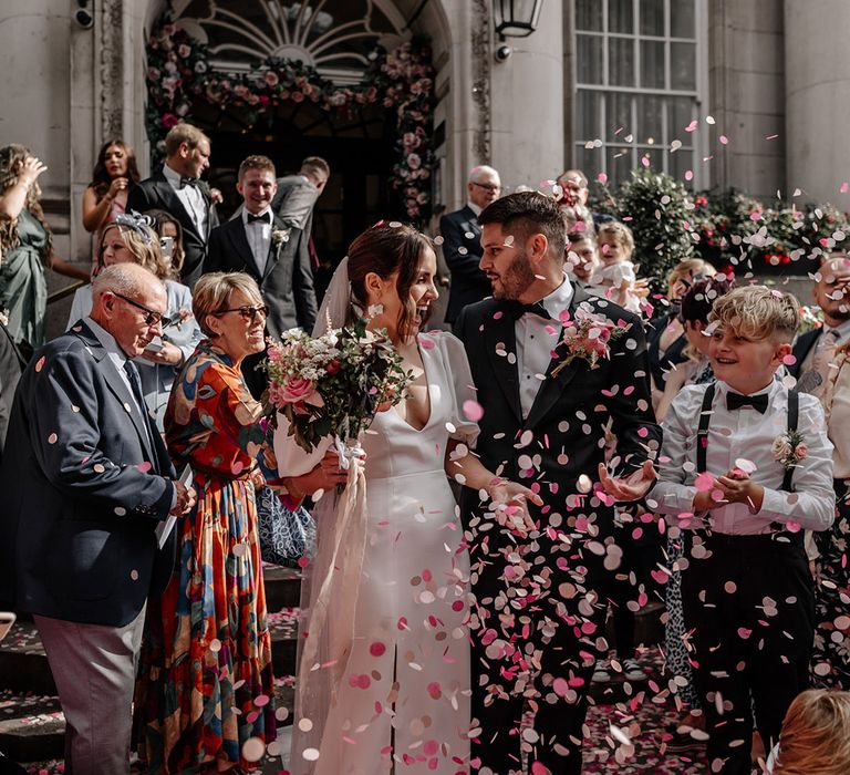 Bride in satin v neck wedding dress with puff sleeves and groom in black tux doing confetti walk at Somerset House wedding