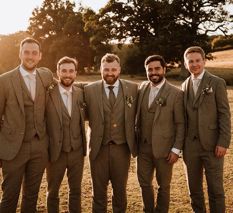 The groom and the groomsmen during golden hour all in matching grey tweed three piece suits