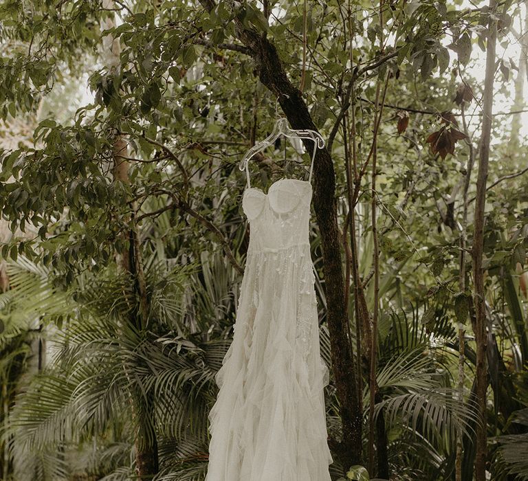 Wedding dress with corset styled bodice and ruffled skirt hangs outdoors 