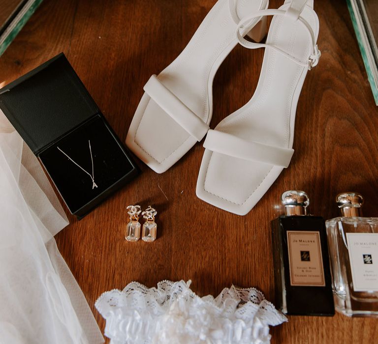 Square toe plain white shoes with Chanel earrings, initial necklace, Jo Malone perfume, and garter for the bride 