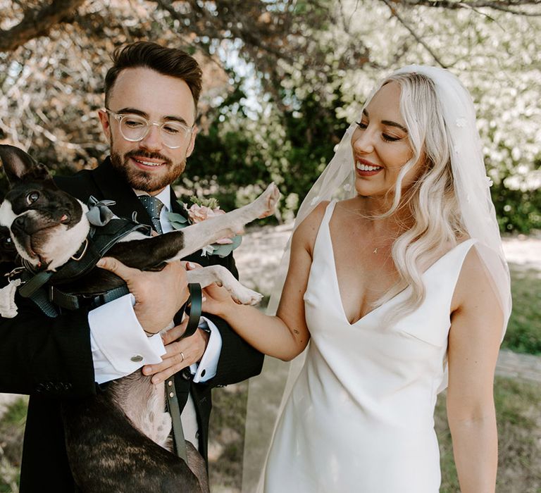 The bride and groom give their pet dog some love who wears a bow tie 