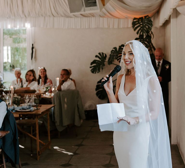 Bride in a white Made With Love wedding dress with a flower applique veil reading out her speech