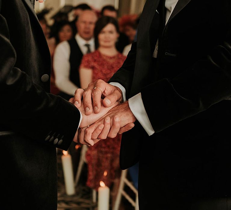 Grooms in matching black velvet blazers holding hands at the alter at The Balmoral Edinburgh 