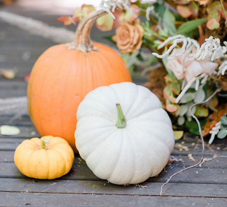 White, yellow and orange pumpkin decor in front of wedding florals 