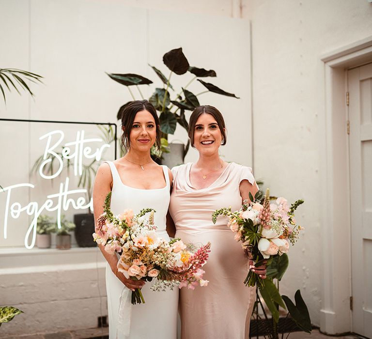 Bride in square neck sleeveless satin wedding dress and bridesmaid in light pink satin cowl neck bridesmaid dress