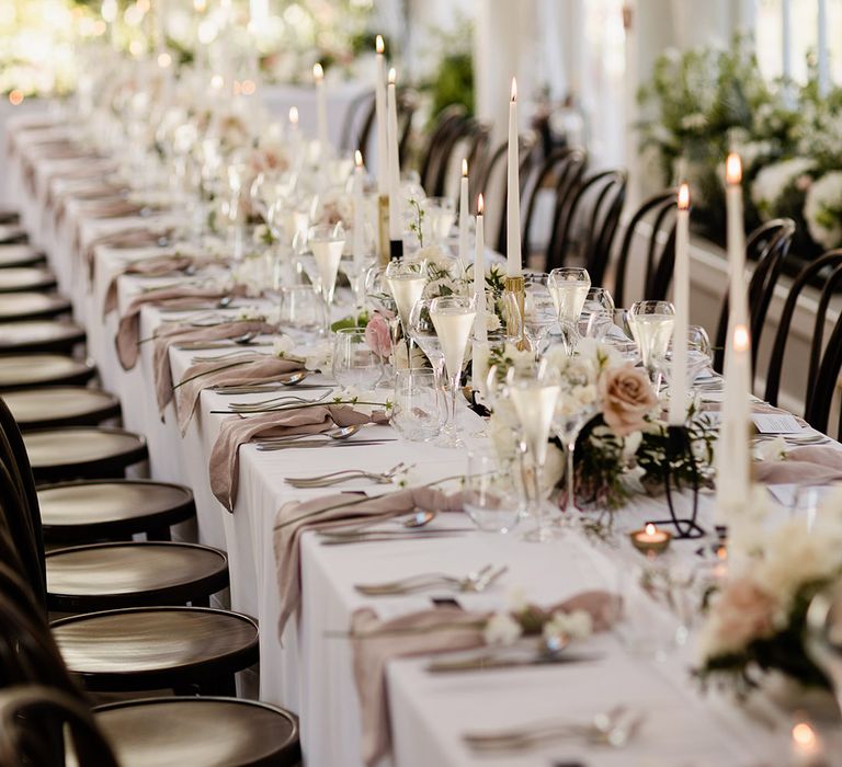 Small floral arrangements line banquet table covered with white tablecloth and fabric pink napkins 