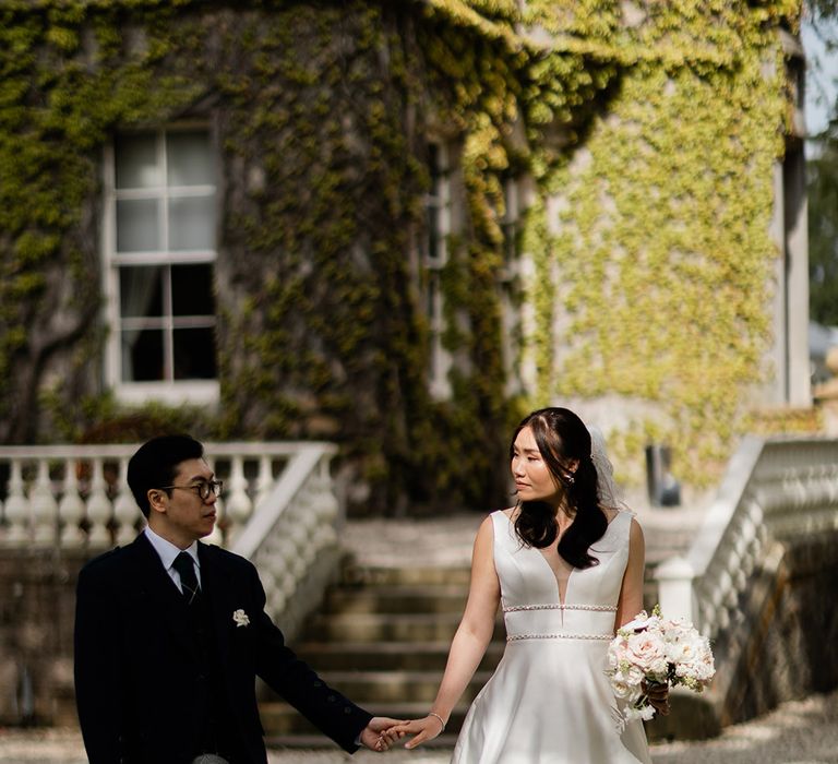 Bride wears Princess wedding dress with embellishment to the waistband and walks alongside her groom in tartan green kilt