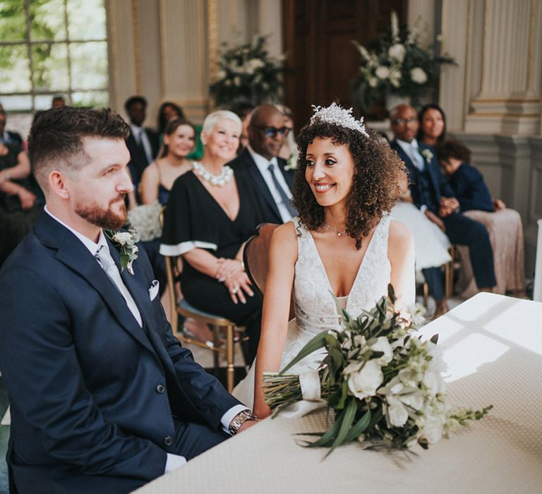 Bride in bridal crown looks lovingly toward her husband during wedding ceremony at Orleans House Gallery