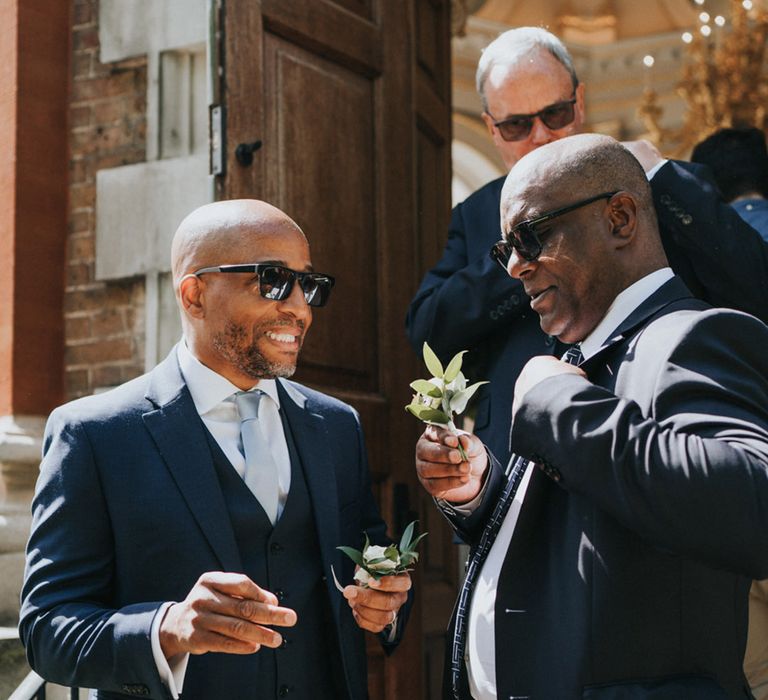 Wedding guests wear three piece suits and floral buttonholes and sunglasses 