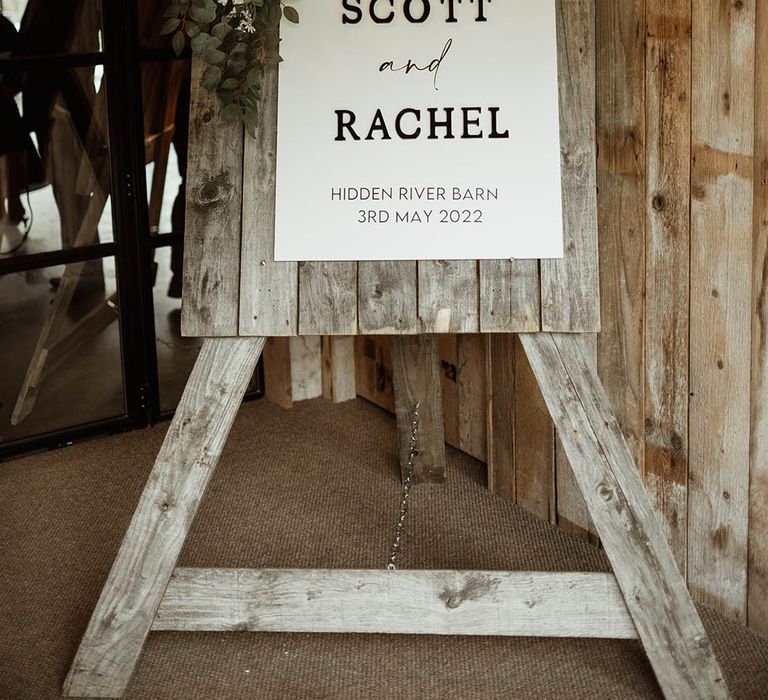 Rustic wedding welcome sign on wooden board with white roses decorating the sign 