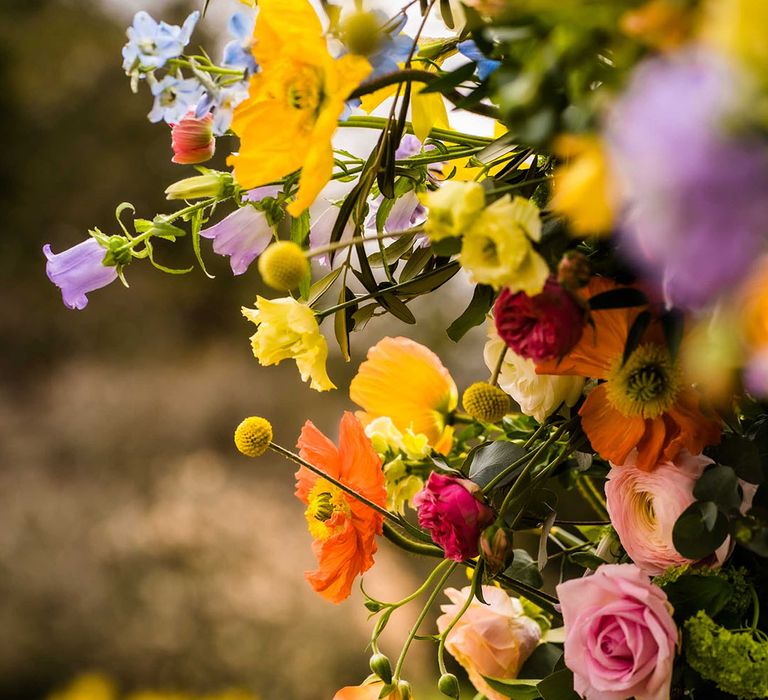 Spring flowers in yellows and oranges within floral archway finished with green foliage 