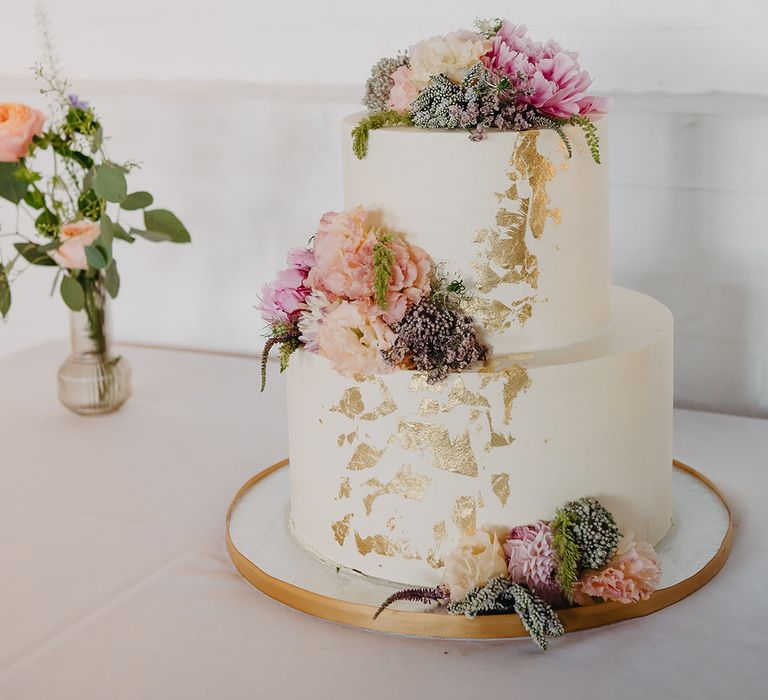 Two tier white frosted wedding cake complete with colourful floral decor and gold leaf 