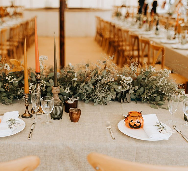 Autumnal leaf table runner arrangement with orange, yellow and black taper candles in gold holders with white plates and mini pumpkin wedding favours 