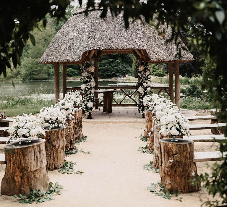 Tree trunk stumps at the end of the benches for outdoor wedding decorated with all white flowers and eucalyptus leaves 