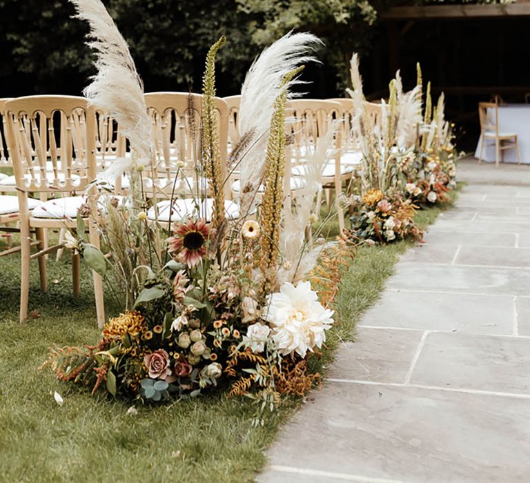 Tall wedding flower aisle decoration with tall pampas grass, foliage, and neutral colour wedding flowers for outdoor wedding 