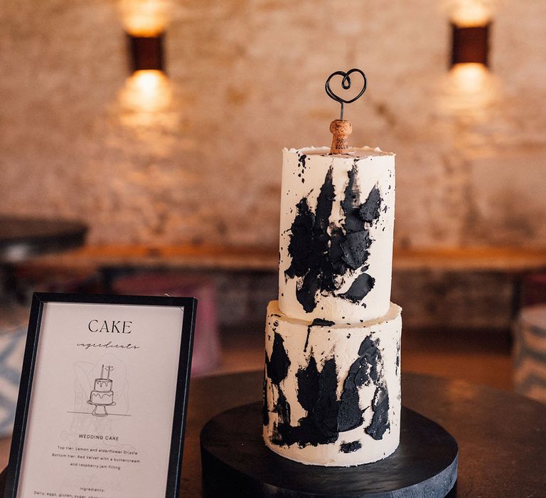 Two tier wedding cake iced with buttercream and black icing with the top layer having lemon and elderflower notes and the bottom being red velvet