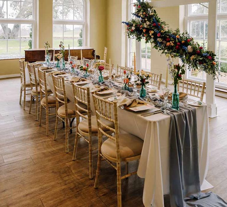 Classic wedding tablescape at Braxted Park wedding venue with white wedding tablecloth, cornflower blue wedding table runner, bright blue glass bottles with dried flowers, pastel tapered candles and spring floral arrangements 