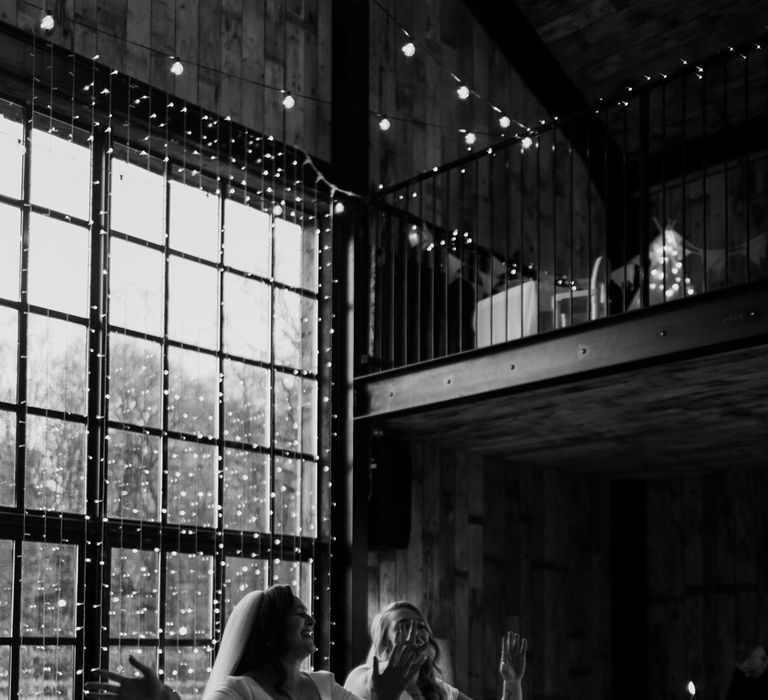 Bride in long sleeve deep v wedding dress and church length veil and bride in satin short sleeve deep v wedding dress and church length veil amidst fairy lights and festoon lighting in Hidden River Cabins reception room 