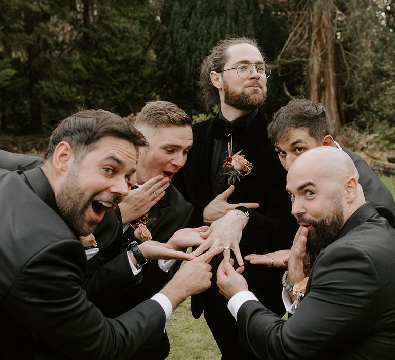 Groom in an all black velvet suit showing off his wedding ring to the groomsmen